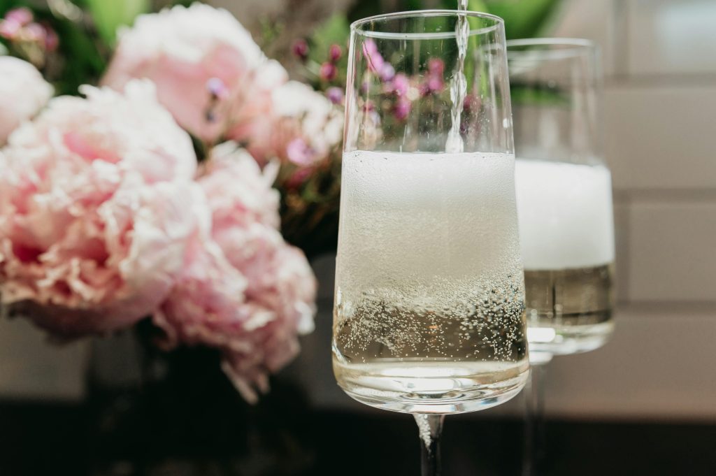 Close-up of sparkling champagne being poured into a glass with peonies in the background.