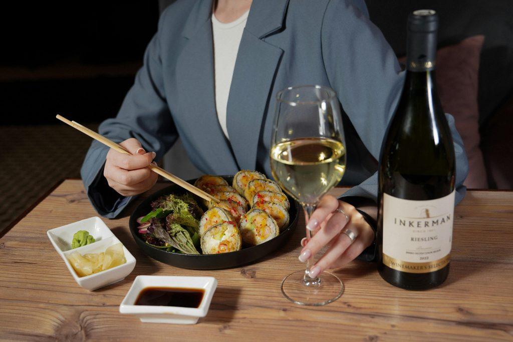 A woman enjoying sushi with white wine, showcasing a sophisticated dining experience.