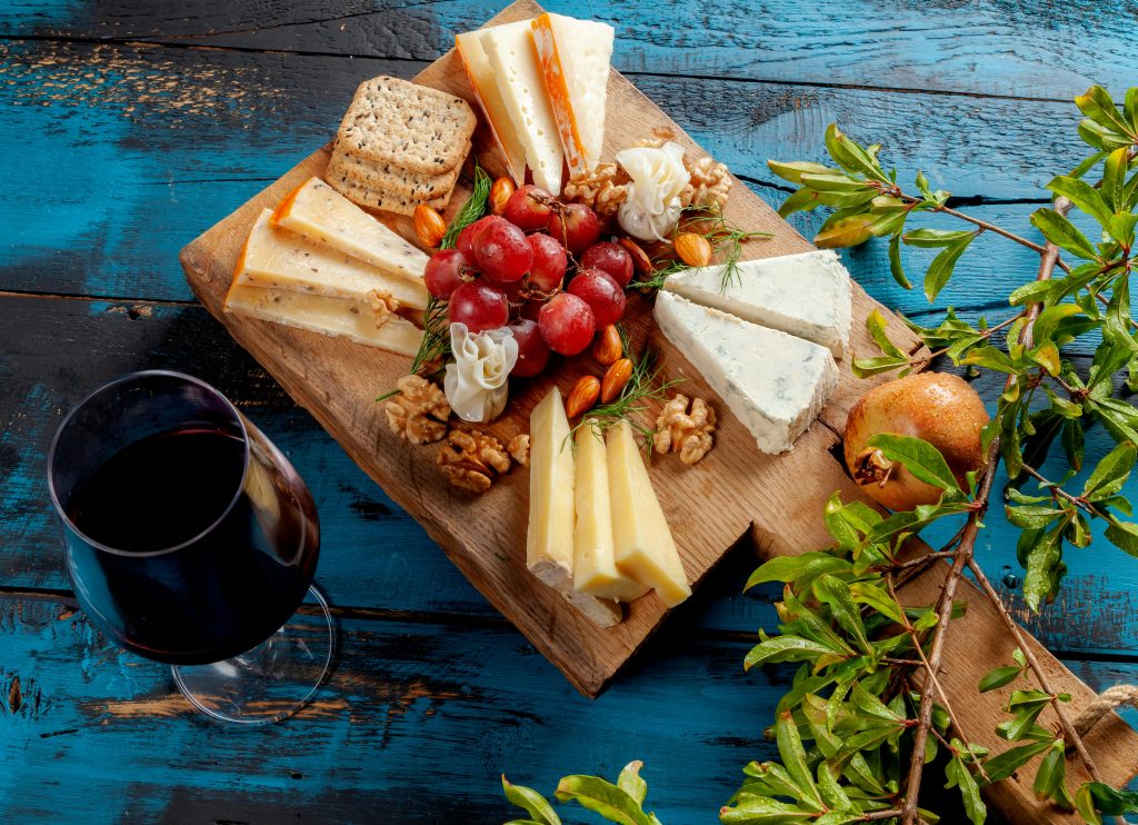 Artistic cheese board with red wine, nuts, and fruits on a blue table.
