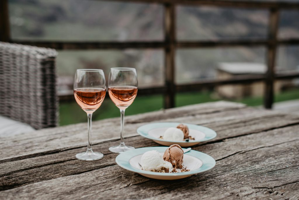 Rustic wooden outdoor table with two glasses of rosé wine and dessert plates featuring chocolate and vanilla ice cream.