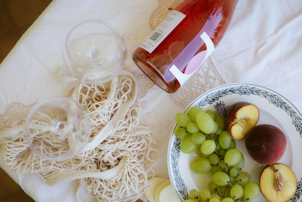 Rosé Wine Guide: Everything You Need to Know A refined picnic scene featuring wine, green grapes, and peaches on a decorative tablecloth.