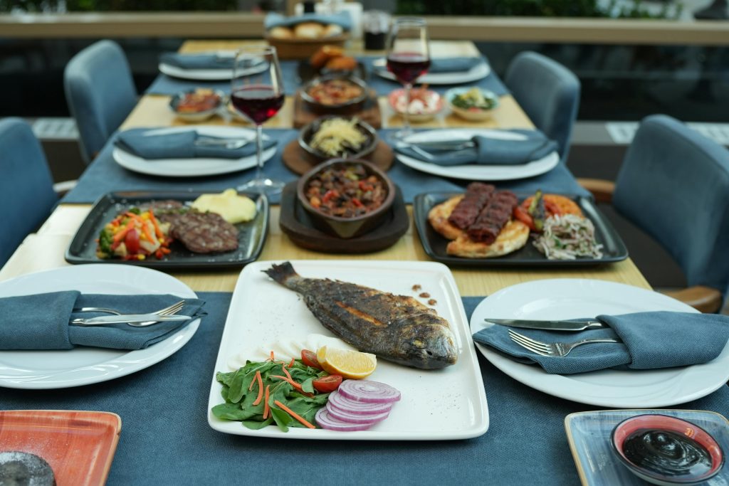 An elegant al fresco dining setup featuring grilled fish, side dishes, and red wine, perfect for a gourmet meal.