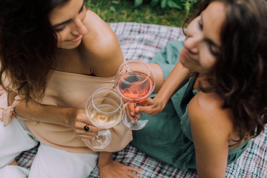 Rosé Wine Guide: Everything You Need to Know Two women enjoying a casual outdoor gathering while toasting with glasses of wine.