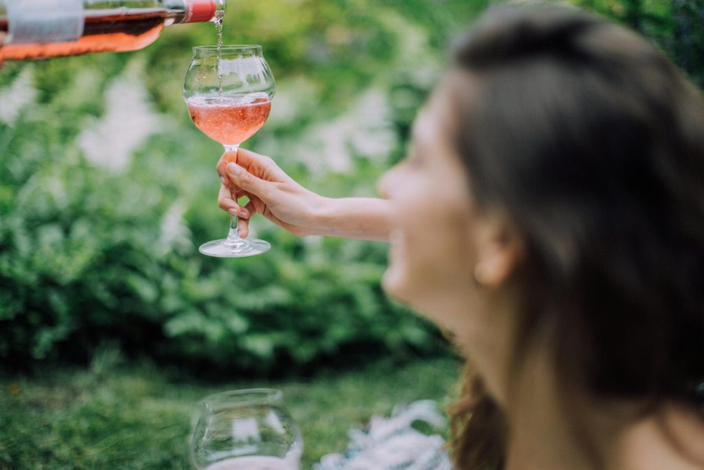 Rosé Wine Guide: Everything You Need to Know A woman elegantly pours rosé wine into a glass during a sunny outdoor picnic, capturing a relaxed summer vibe.