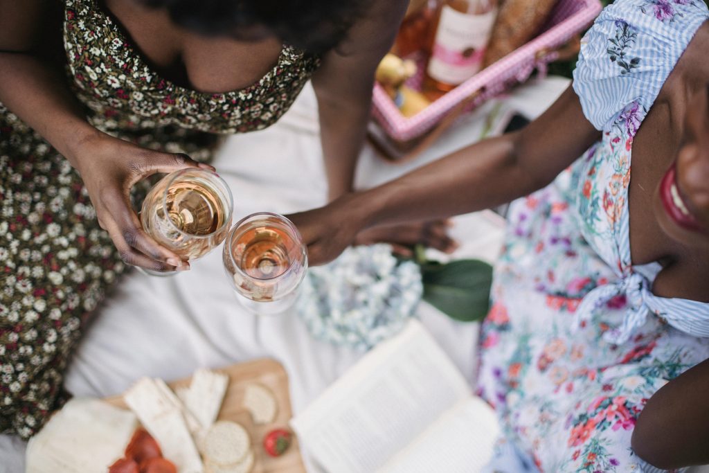 A close-up, top view of two women enjoying wine and snacks at an outdoor picnic.