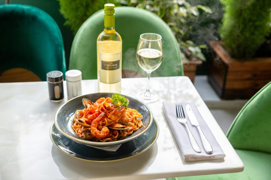 A plate of seafood pasta with white wine on a marble table in a sophisticated setting.