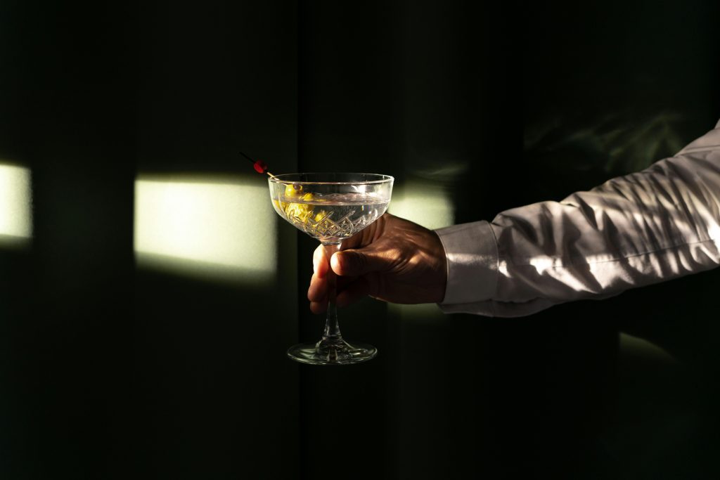Sophisticated martini cocktail held in hand with striking light effects on a dark background.