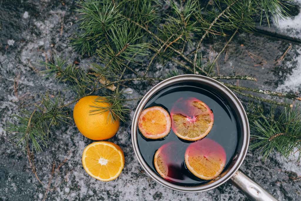 Flat lay of mulled wine with orange slices and pine branches, evoking a cozy winter feel.