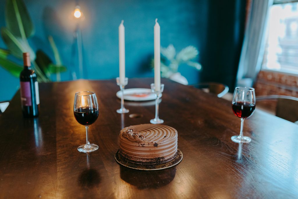 A sophisticated table setup featuring a chocolate cake, red wine, and candles on a wooden table.