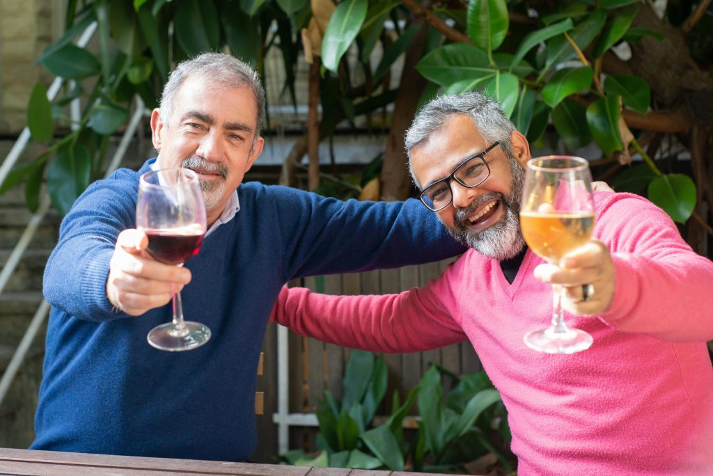 Two senior men enjoying wine and friendship outdoors, smiling and celebrating.