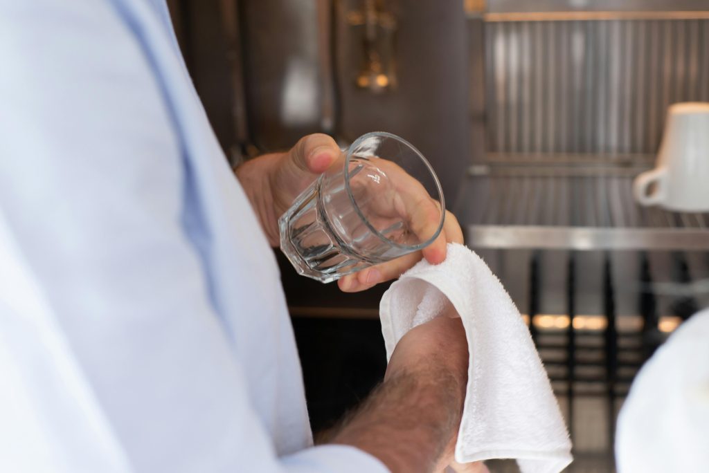 A person drying a glass with a towel in an indoor kitchen setting.