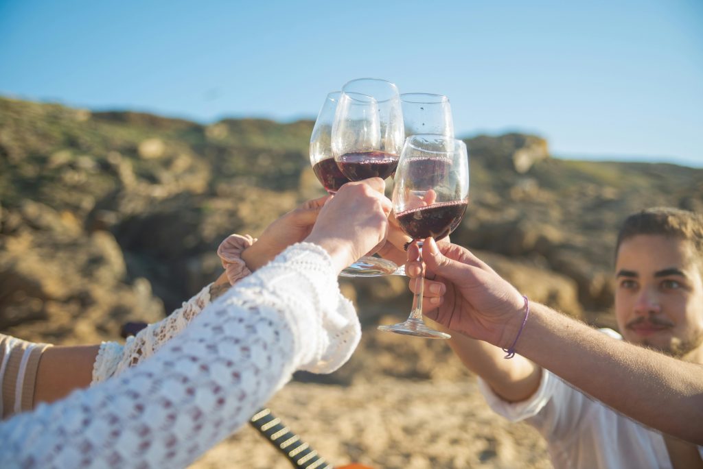 Friends toasting with red wine outdoors in a sunny Portuguese landscape.