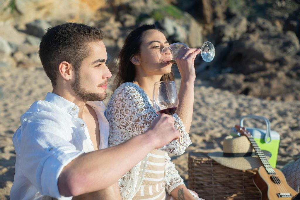 Couple enjoying a picnic with red wine on a sunny beach in Portugal.