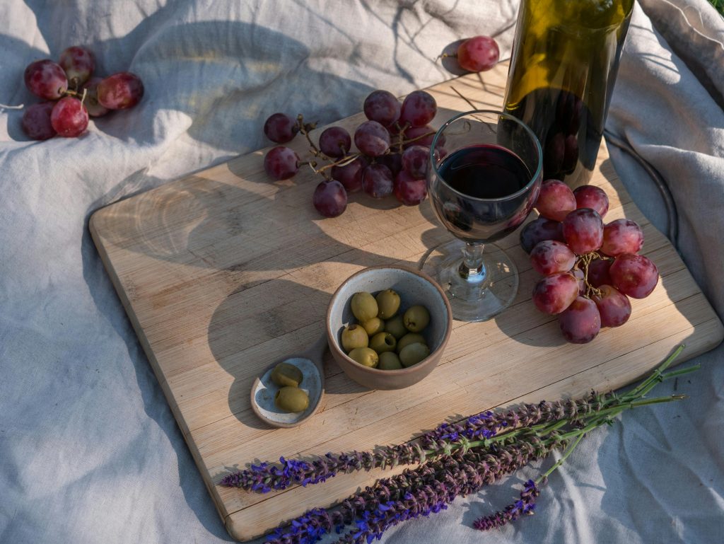 Is Wine Vegan? What Every Wine Drinker Should Know A cozy picnic setup featuring wine, red grapes, olives, and lavender on a wooden board.