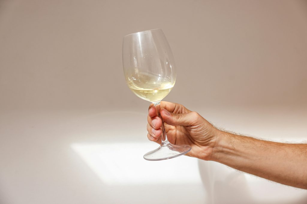A close-up of a hand holding a glass of white wine against a plain white background, emphasizing elegance.