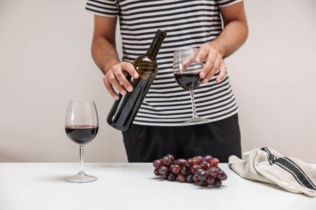 How to Pair Wine With BBQ: 5 Simple Rules Adult pouring red wine into glass, grapes on table. Elegant and inviting indoor scene.