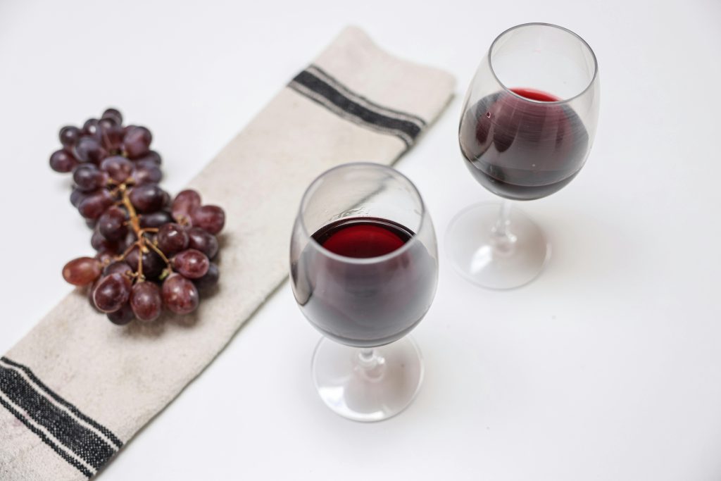 Two wine glasses and a bunch of grapes elegantly arranged on a white table with a napkin.