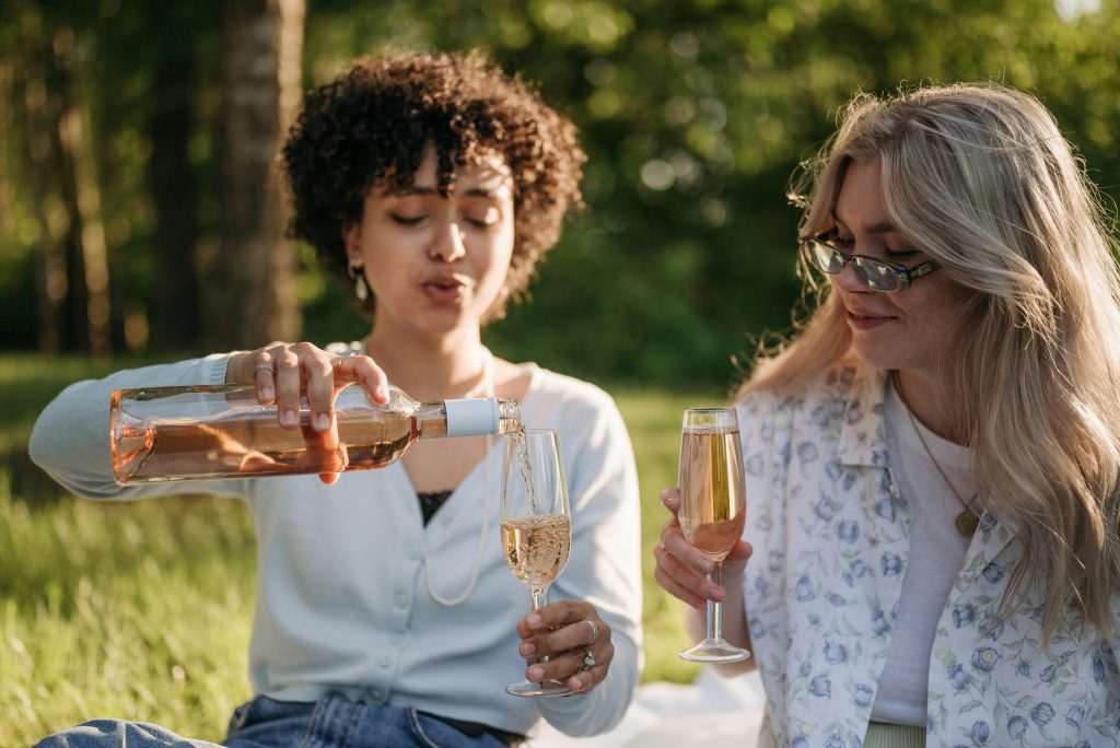 Rosé Wine Guide: Everything You Need to Know Two women having a picnic, pouring rosé wine outdoors in a relaxing setting.