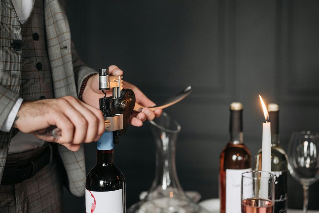 Man elegantly opening a wine bottle with a corkscrew at a candlelit dinner setting.