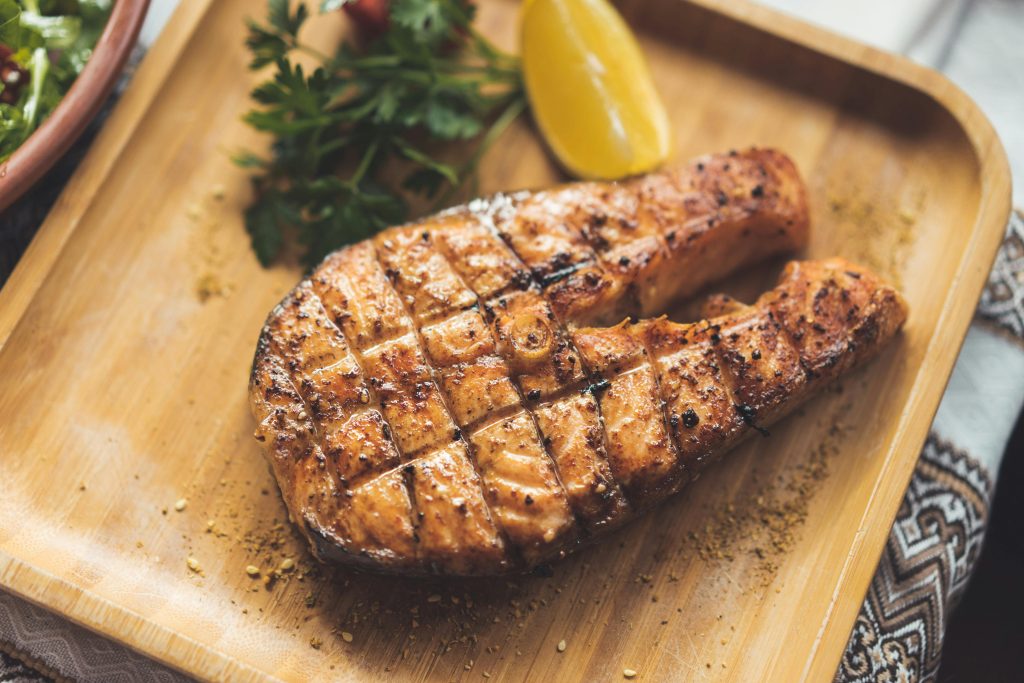 Wine and Salmon Pairing: The Complete Guide Close-up of seasoned grilled salmon steak with lemon and herbs on a wooden platter.