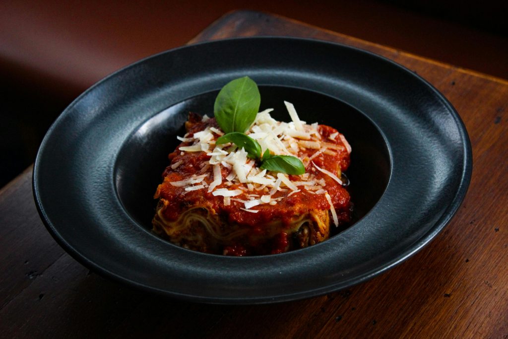 Close-up of a delicious lasagna served in a black plate, garnished with cheese and basil.