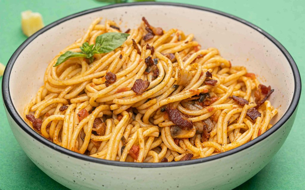 Close-up of a spaghetti dish with bacon and herbs, vibrant culinary presentation.