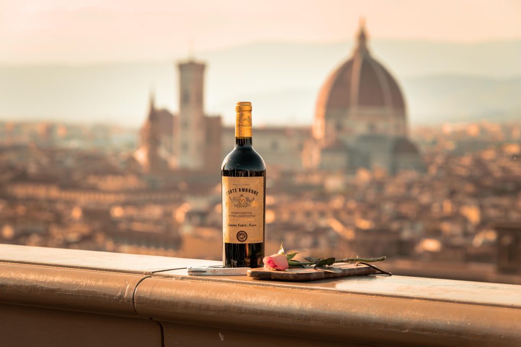 A wine bottle on a balcony overlooking the Florence skyline with the iconic Duomo in the background at sunset.