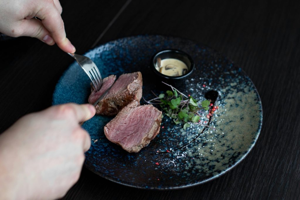 Wine and Steak Pairing: Best Bottles for Every Cut Close-up of a gourmet steak being sliced on a blue ceramic plate with sauce.