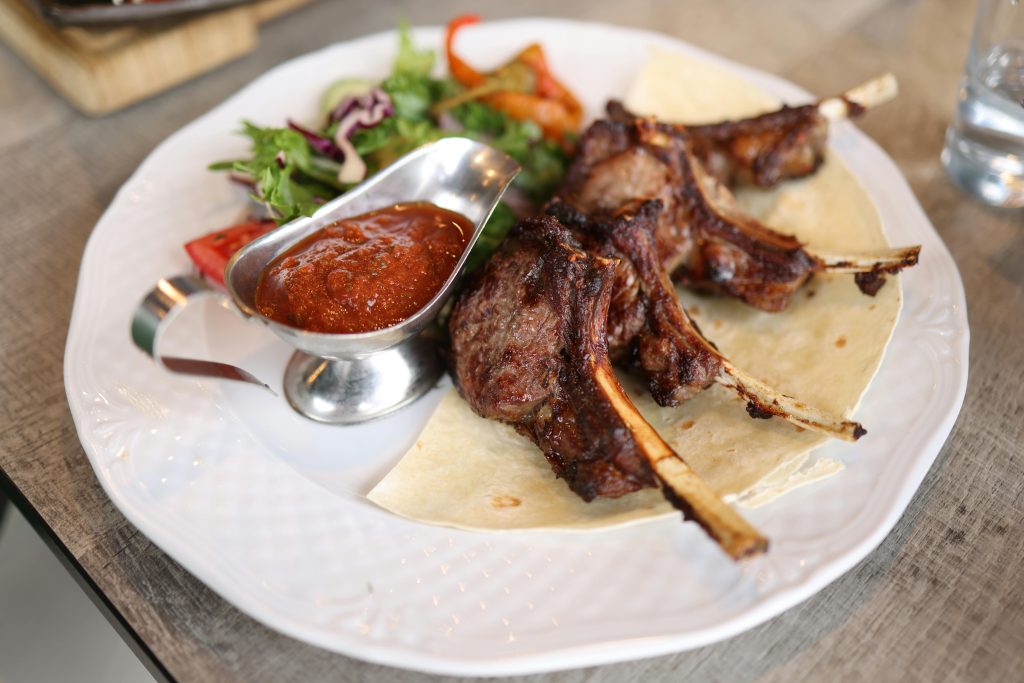 Juicy roasted lamb chops served with fresh salad and spicy sauce on a plate.