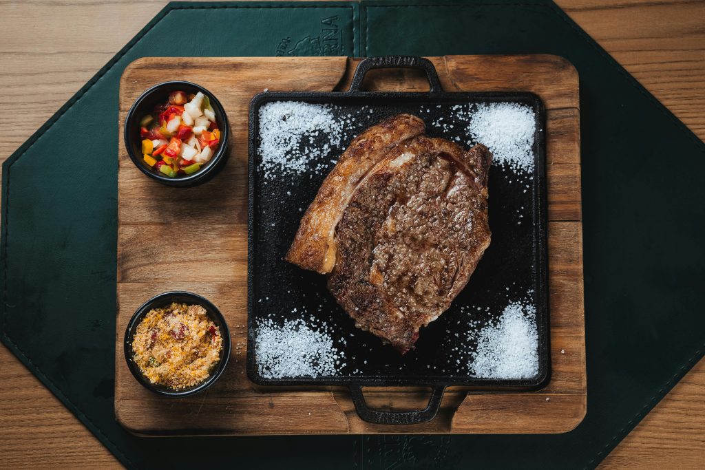 Wine and Steak Pairing: Best Bottles for Every Cut Delicious grilled ribeye steak with colorful salsa and farofa served on a wooden board.