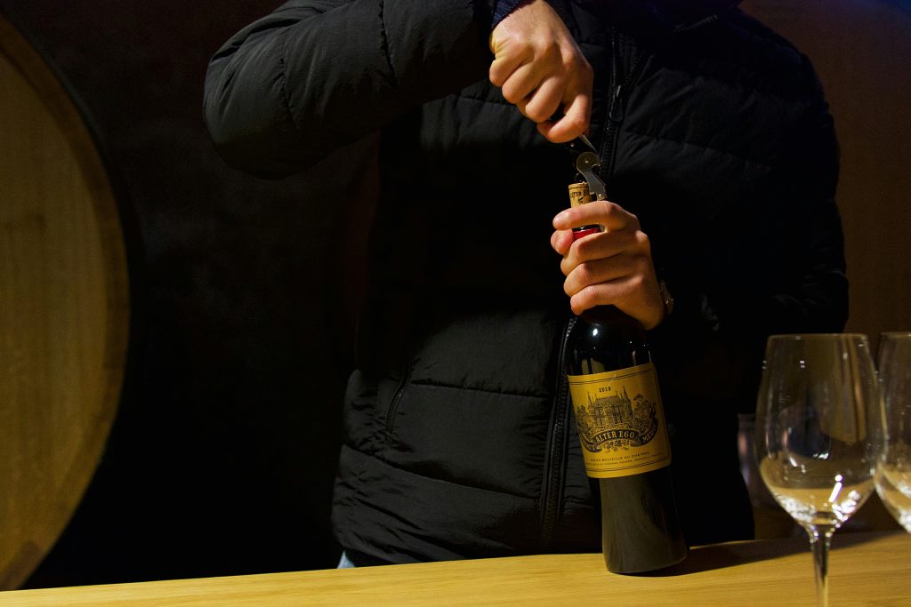 Best Bordeaux Wines Under $50 Person uncorking wine bottle in Margaux, Bordeaux. Elegant wine tasting in a French cellar.