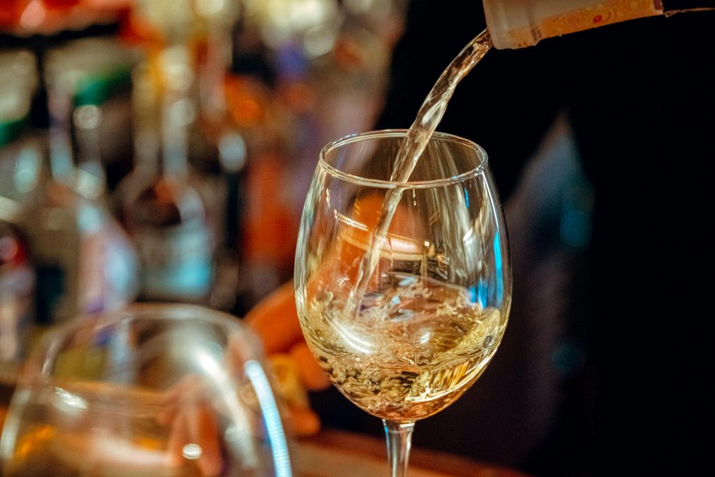 A close-up of white wine being poured into a glass in a lively Ankara pub.