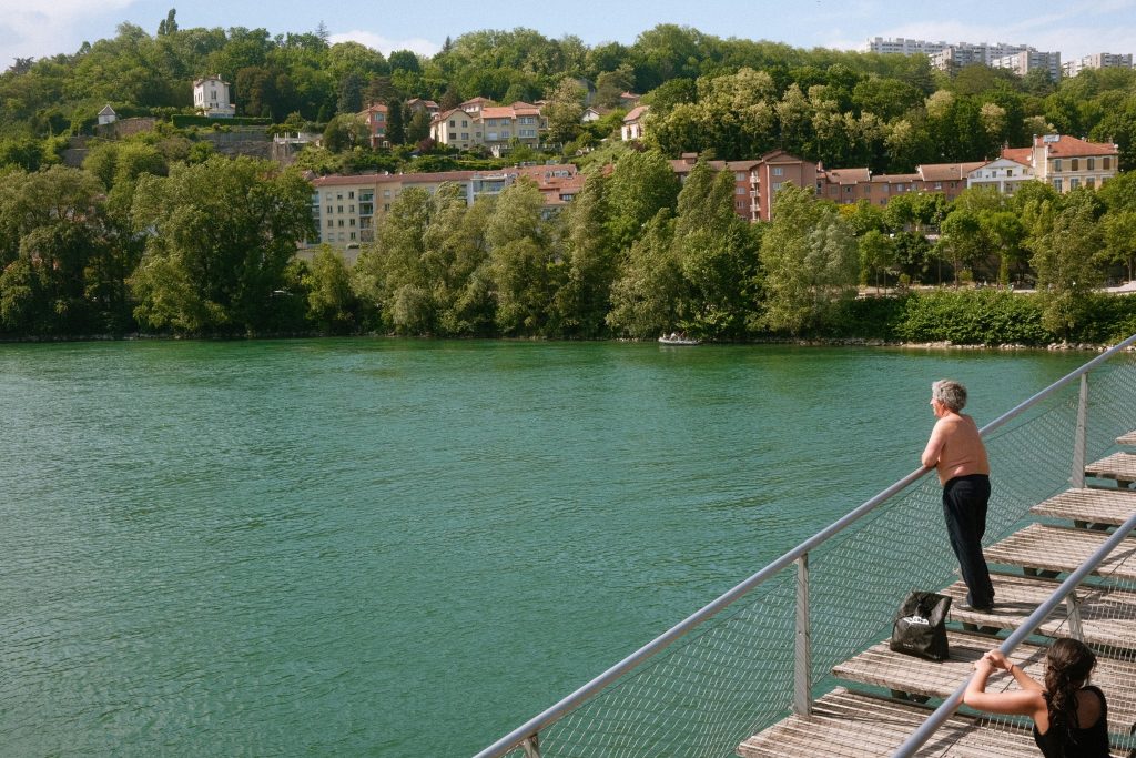 Adult enjoying a peaceful view across the Rhône River in Lyon, framed by lush greenery and urban architecture.