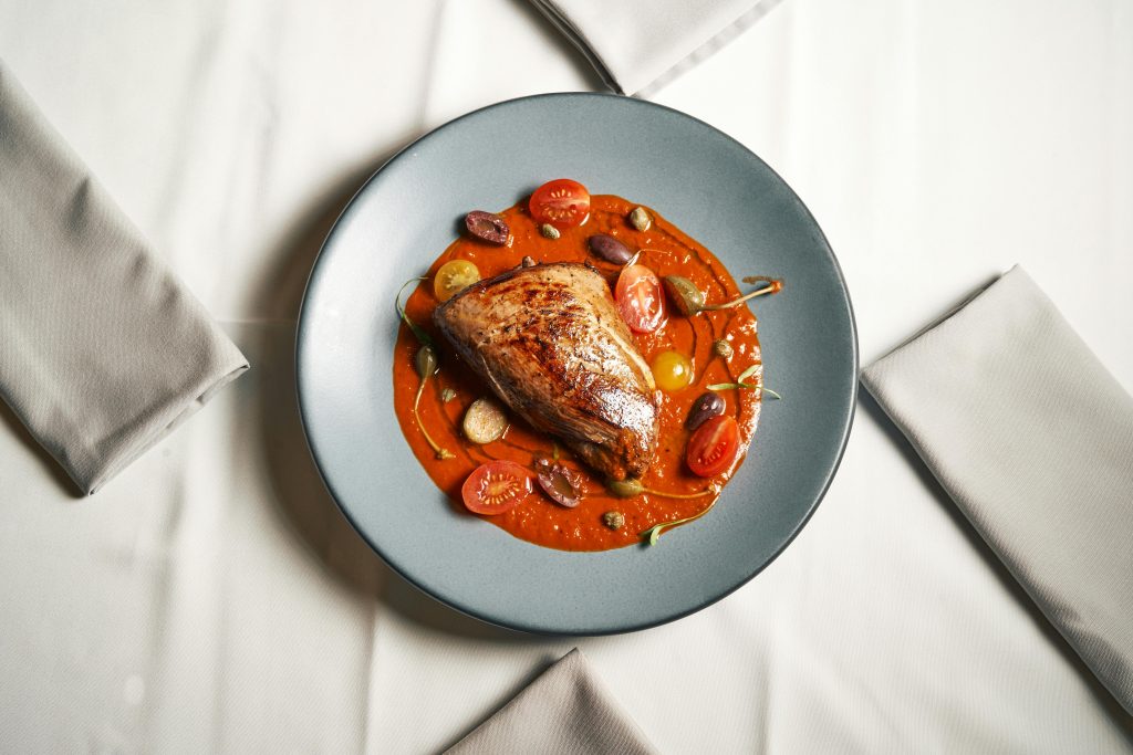 Delicious roast chicken breast served on a bed of vibrant tomato sauce with cherry tomatoes and olives.