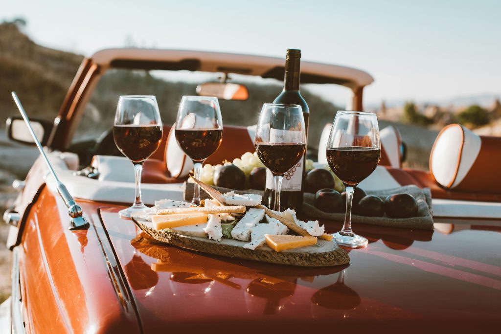 A scenic outdoor picnic with wine glasses and cheese on a vintage car trunk.