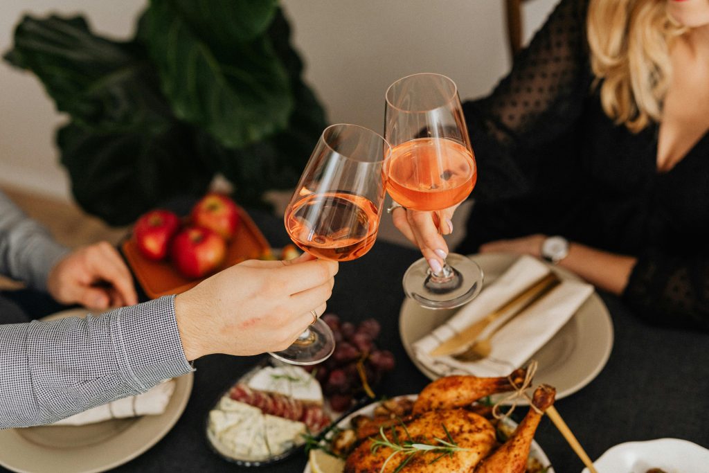 Best Wines for a Summer BBQ Couple toasting with wine over a delicious roasted chicken dinner.