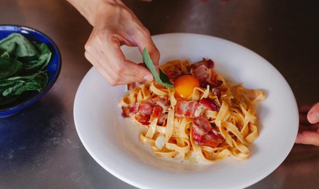 Delicious carbonara pasta with bacon and egg yolk garnished with fresh basil. Perfect for food lovers.