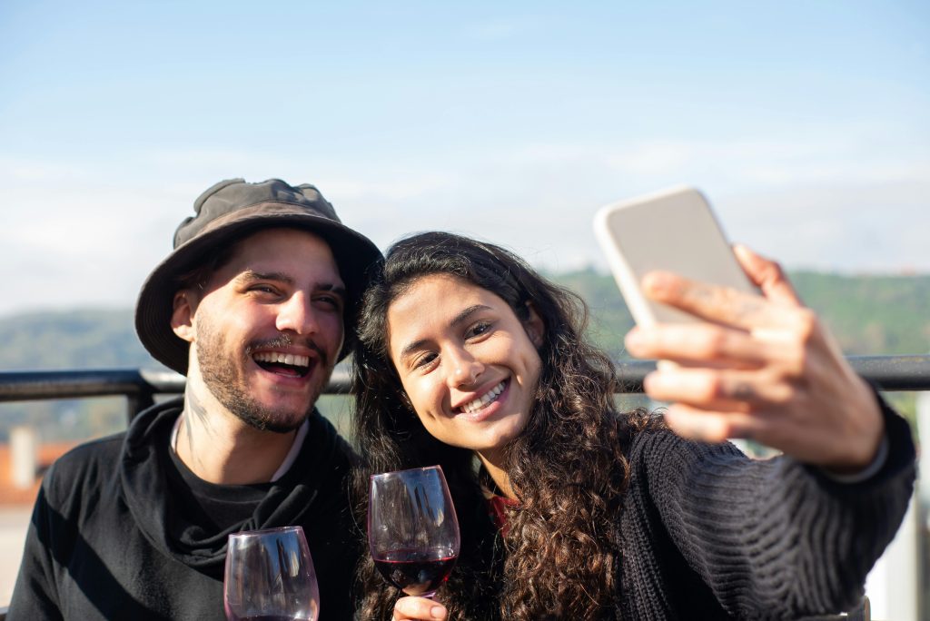 Smiling couple enjoying wine and taking a selfie outdoors in Italy.