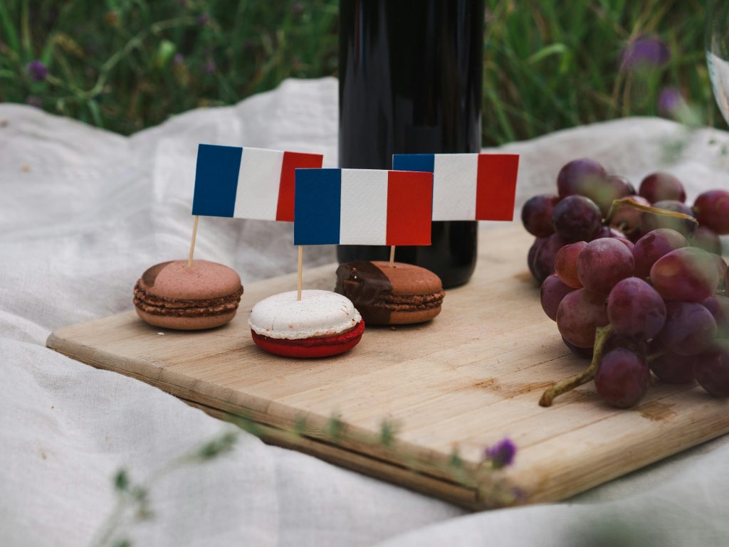 Macarons decorated with French flags on a picnic setup with grapes and wine.