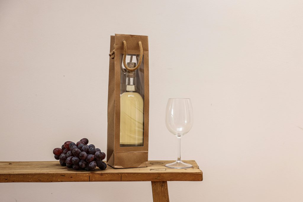 Best Bordeaux Wines Under $50 A wine bottle in a paper bag with grapes and an empty glass on a wooden table.