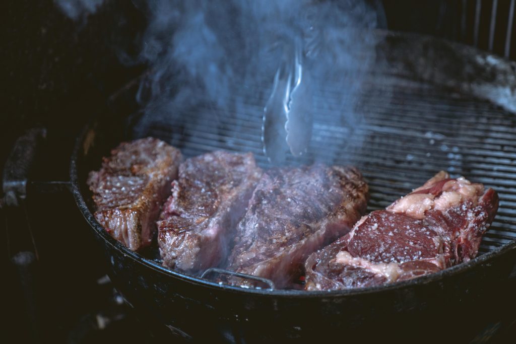 Wine and Steak Pairing: Best Bottles for Every Cut Close-up of juicy steaks sizzling on a smoky barbecue grill, ideal for a food or lifestyle theme.
