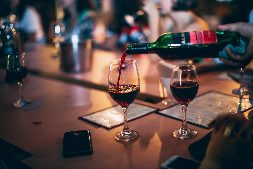 Red wine being poured into glasses at a vibrant bar scene, creating a warm atmosphere.