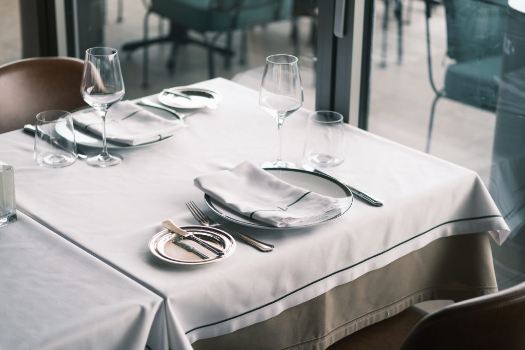 Elegant dining setup with white tablecloths, cutlery, and wine glasses in a modern restaurant.