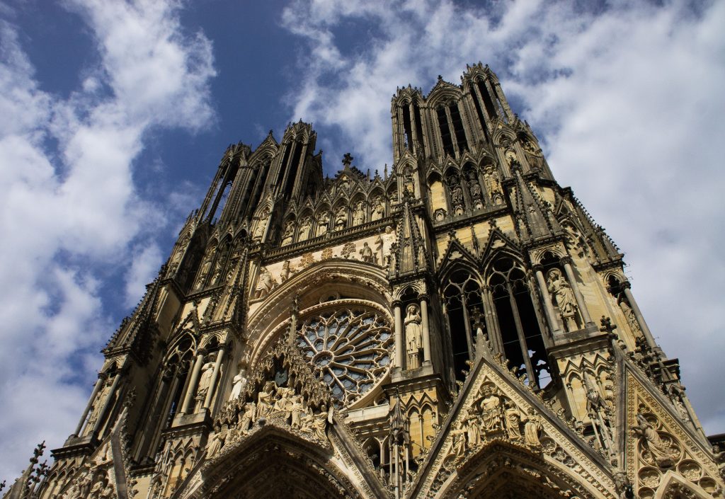 Low angle shot of Reims Cathedral showcasing Gothic architecture against blue sky.