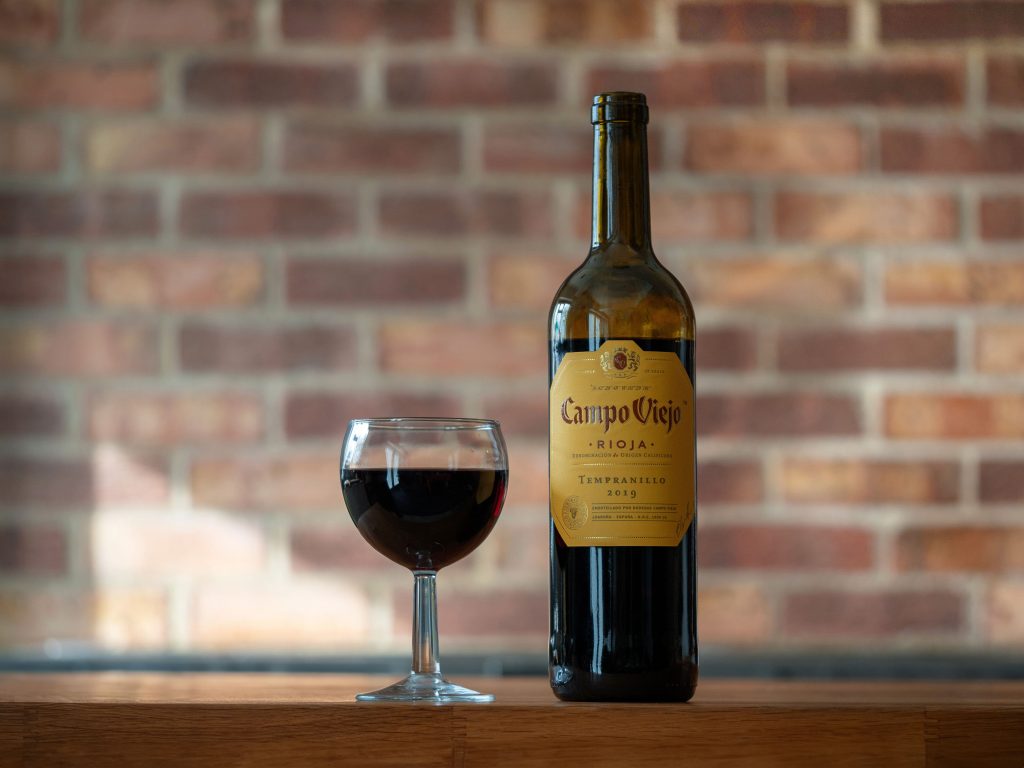 Red wine bottle and glass against brick wall backdrop, perfect for cozy evenings.