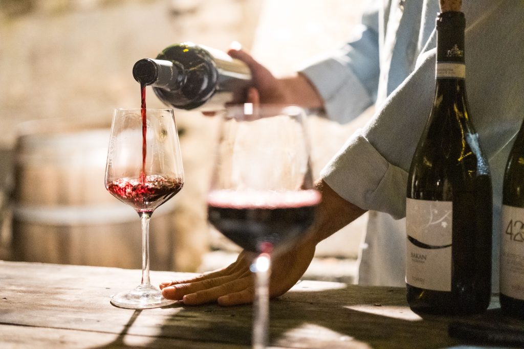 A person pouring red wine into a glass in a rustic, cozy wine bar setting.