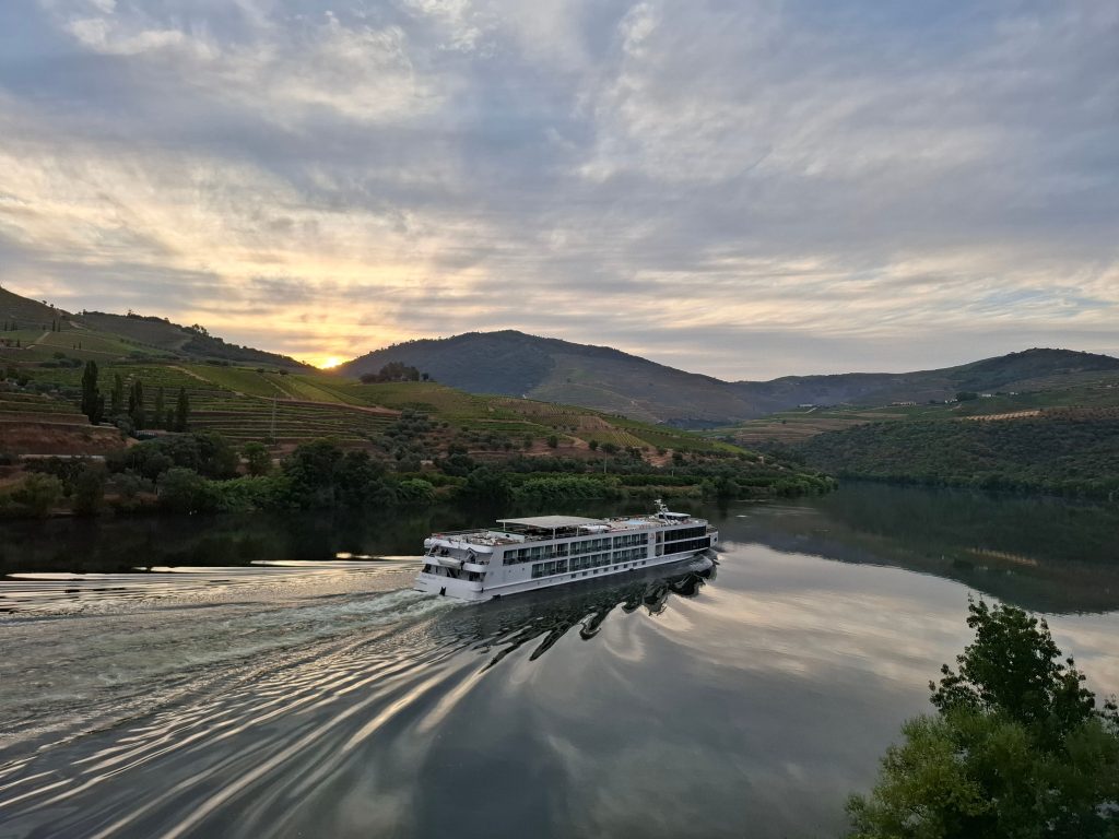 Riverboat cruising through the picturesque Douro Valley at sunset, surrounded by lush vineyards.