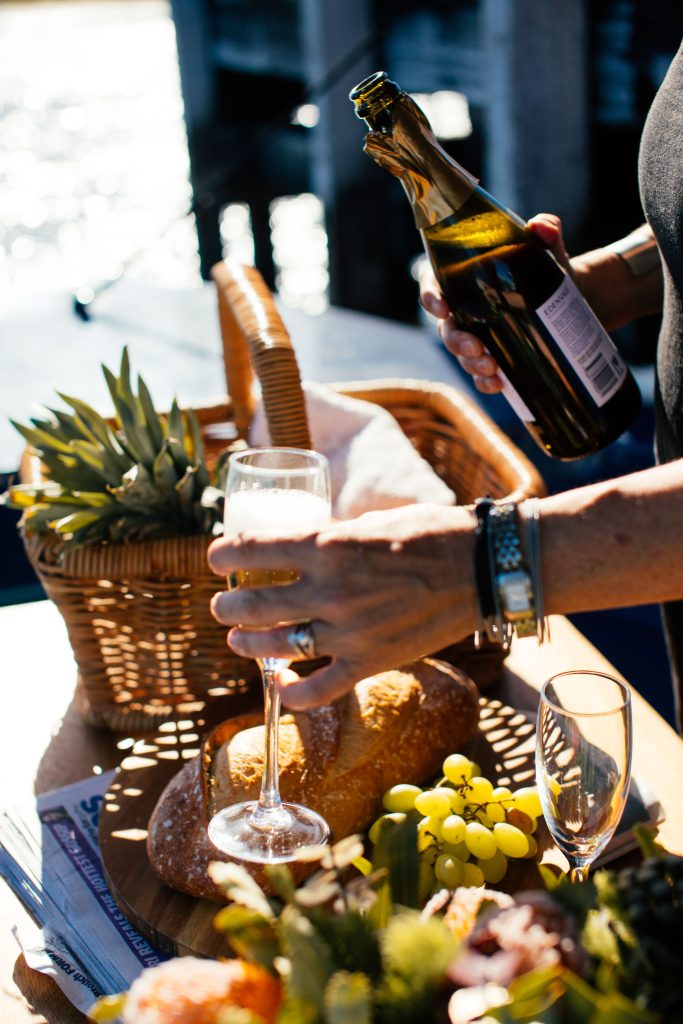 Crop faceless person pouring champagne from bottle into glass while having party on boat