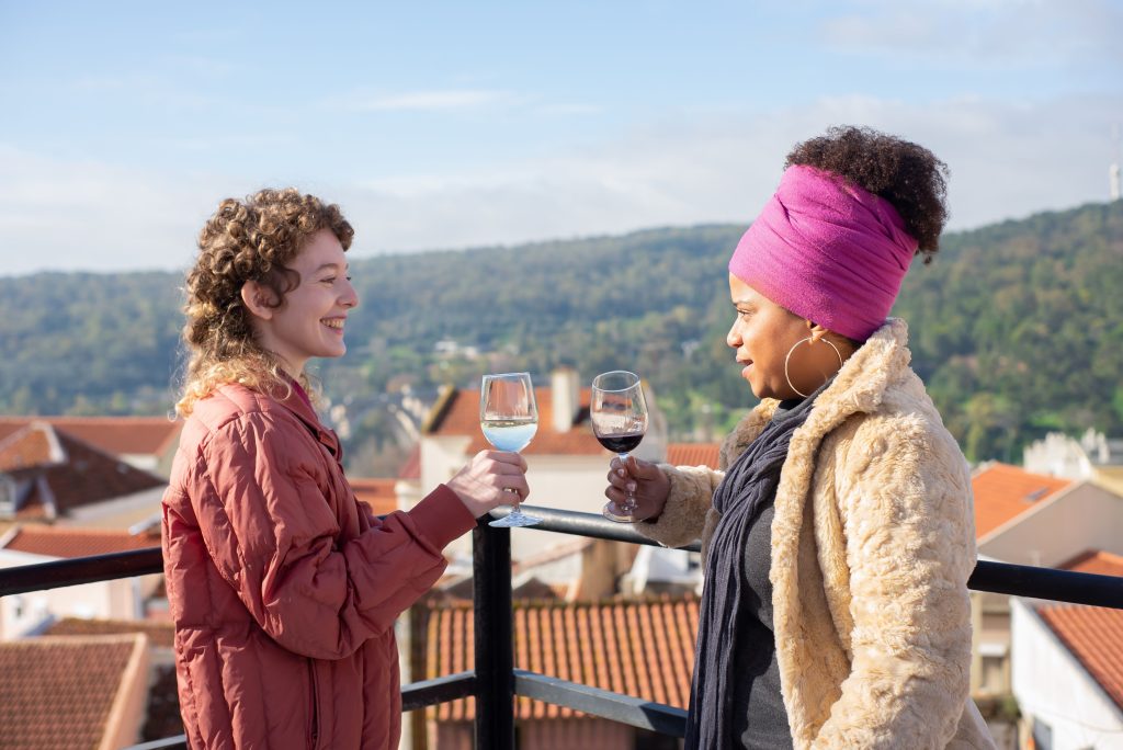 Two women share a joyful moment with wine outdoors overlooking a picturesque view in Portugal.