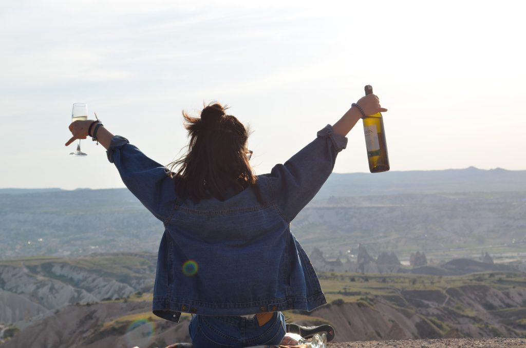 A person celebrates with wine overlooking a stunning scenic view, embracing nature and freedom.